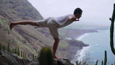 Amidst-the-mountainous-scenery,-a-fit-young-man-practices-sun-salutation-yoga,-absorbing-the-ocean-panorama.-Meditation-and-exercise-converge,-symbolizing-a-dynamic-lifestyle